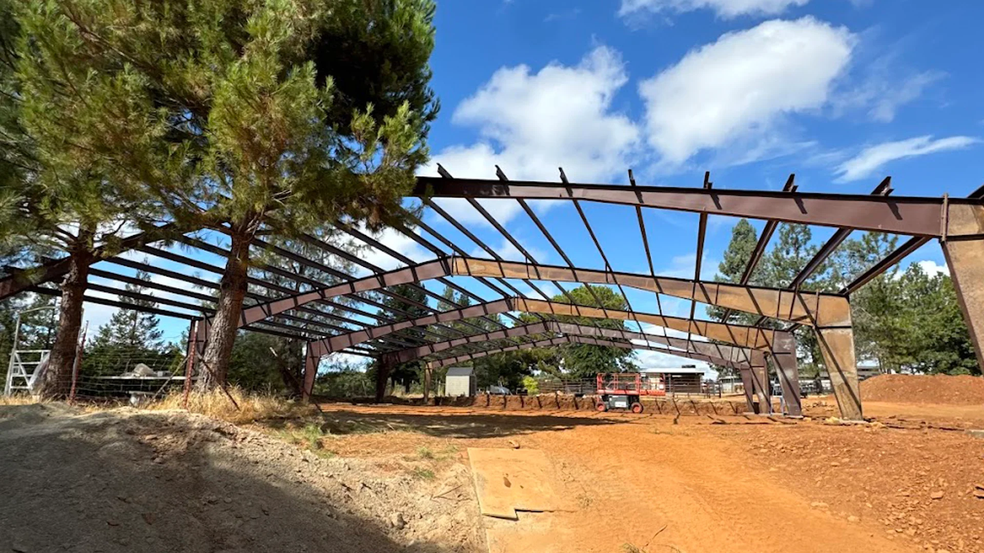 Metal building framework under construction with trees and blue sky, illustrating Ibarra Construction's metal building design services.