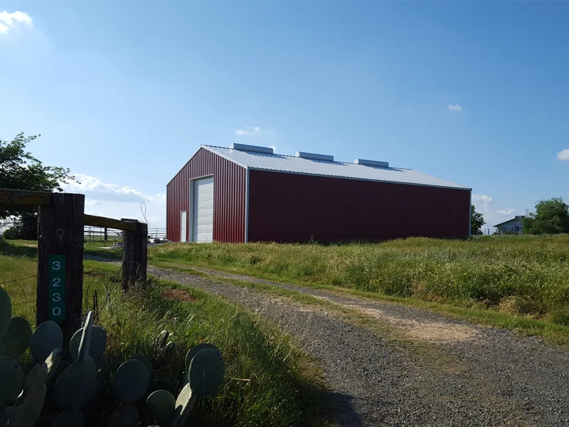 Red metal barn structure with a gray roof, surrounded by green grass and a gravel path, illustrating Ibarra Construction's metal building services.