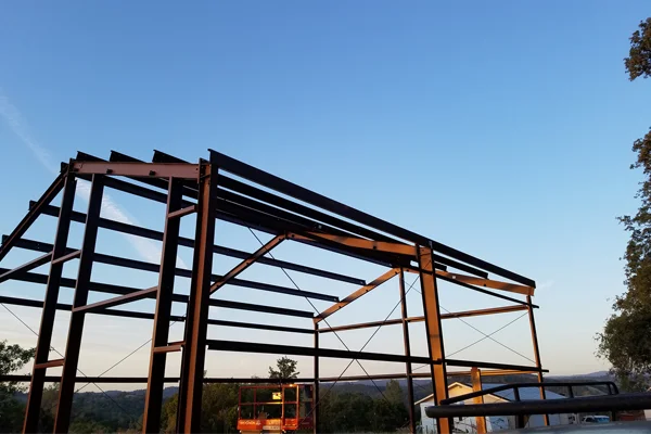 Metal building framework under construction against a clear blue sky, showcasing Ibarra Construction's steel structure services for barns and commercial projects.