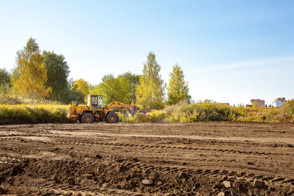 Excavator leveling site for construction preparation, showcasing professional grading services in a cleared area surrounded by trees.
