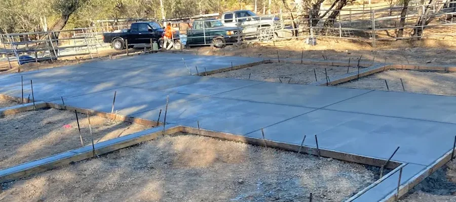Concrete foundation installation in progress, showcasing a smooth concrete slab surrounded by wooden forms, with vehicles and workers in the background, emphasizing Ibarra Construction's site development expertise in Woodland, CA.