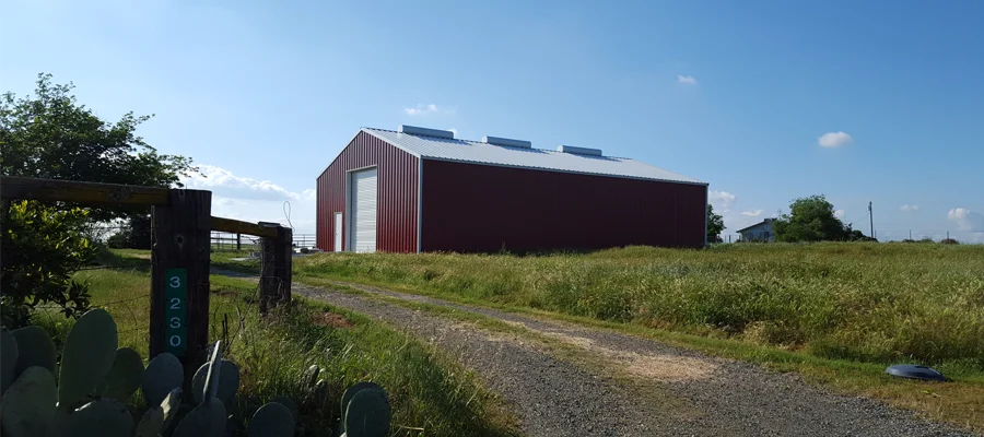 Large red barn with a metal roof set against a clear blue sky, surrounded by green grass and a gravel path leading to the entrance, showcasing Ibarra Construction's expertise in barn construction in Woodland, CA.