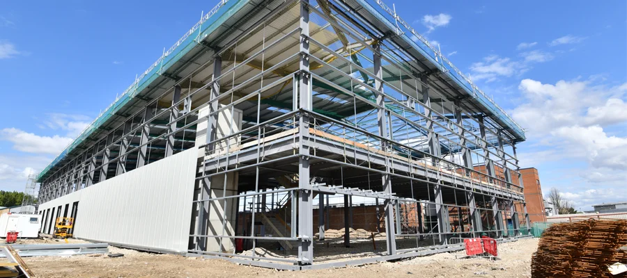 Commercial construction site featuring a steel structure under construction, showcasing scaffolding, exterior wall installation, and a clear blue sky, representing Ibarra Construction's expertise in durable and functional building solutions.