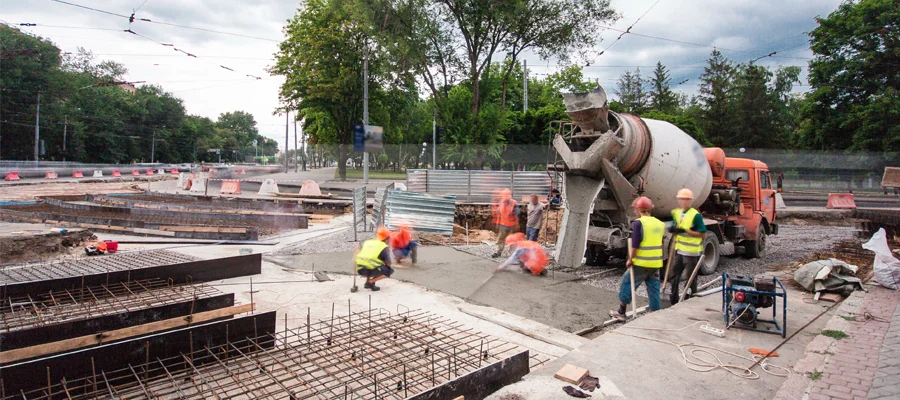 Construction workers pouring concrete at a construction site, with a concrete mixer truck, reinforcing steel bars, and machinery visible, emphasizing the process of building durable structures.
