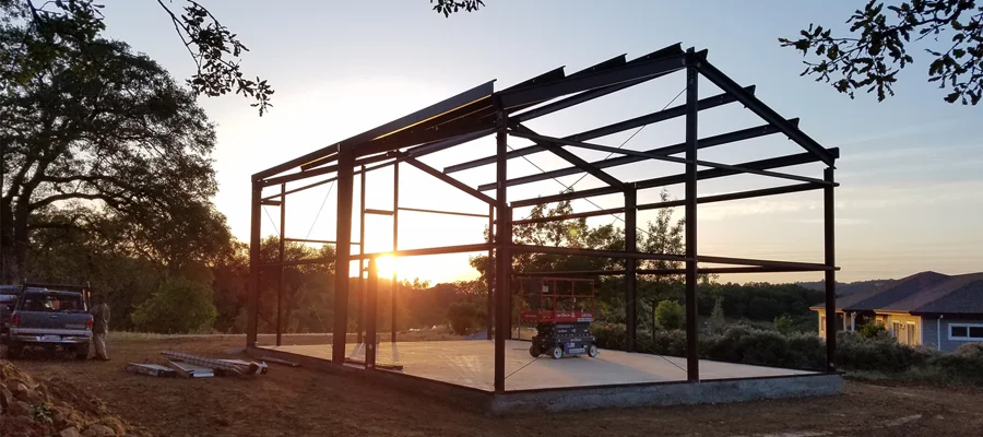 Steel structure under construction with a sunset backdrop, showcasing the framework for a building, emphasizing durability and precision in construction services by Ibarra Construction in Woodland, CA.