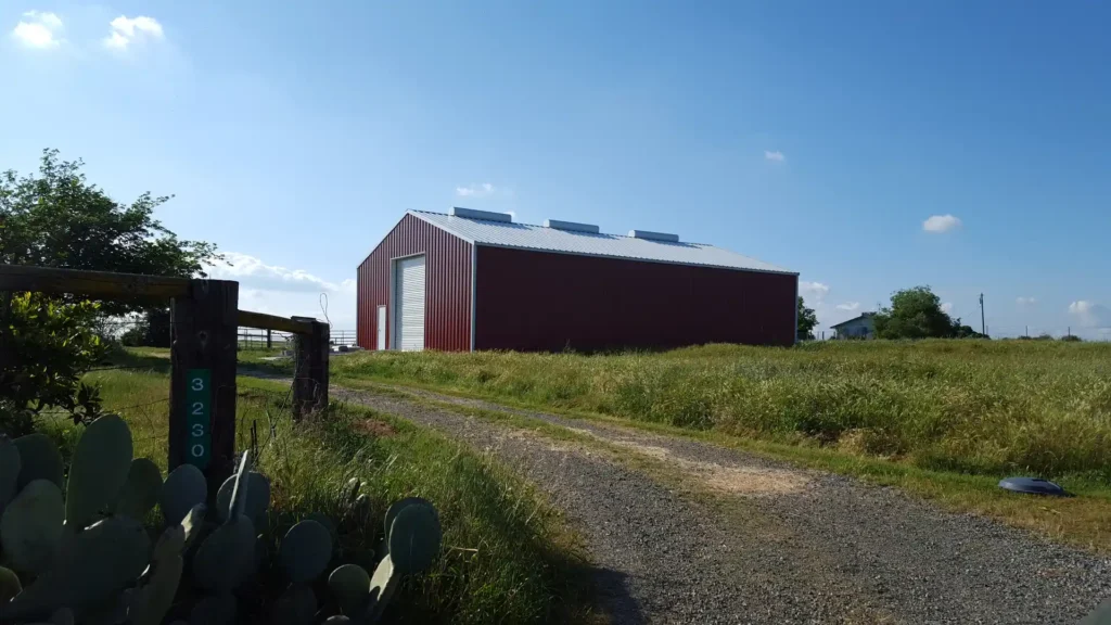 Red metal barn in a rural setting, surrounded by tall grass and cacti, showcasing durability and design flexibility for agricultural use.