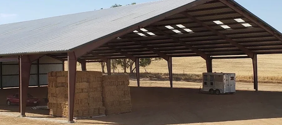 Metal building structure with open design, featuring stacked hay bales, a trailer, and a clear sky, illustrating durable agricultural storage solutions by Ibarra Construction in Winters, CA.