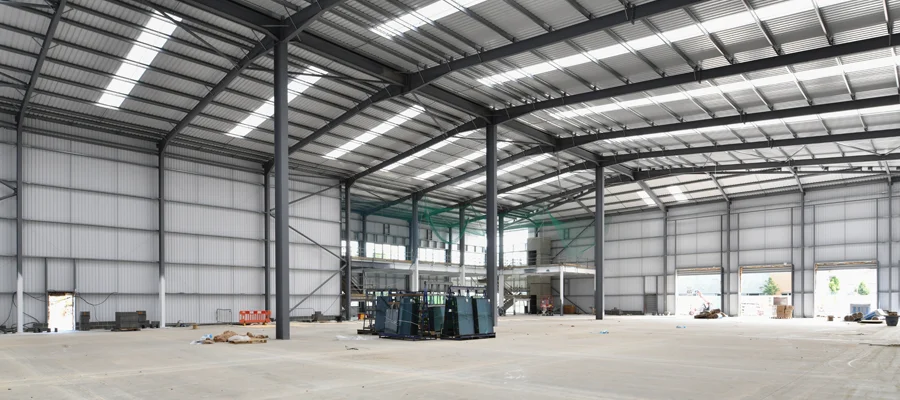 Interior view of a spacious steel structure warehouse, showcasing high ceilings, metal framework, and concrete flooring, emphasizing commercial construction capabilities for agricultural buildings and shop frameworks.