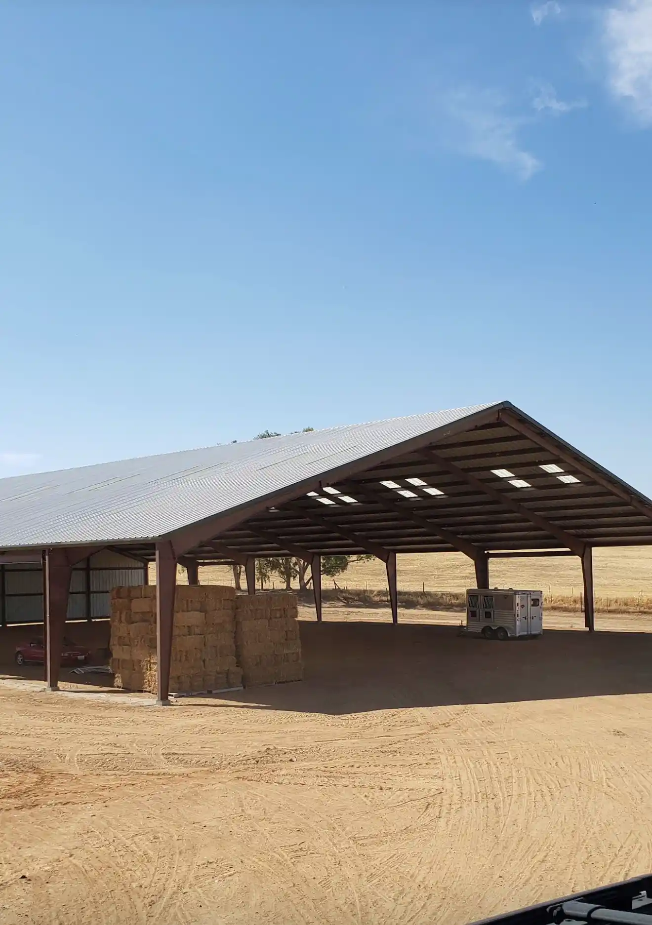 Commercial steel riding arena in Esparto, CA, featuring a large covered structure with a metal roof, concrete foundation, and hay bales stacked nearby, illustrating Ibarra Construction's work on equestrian facilities.