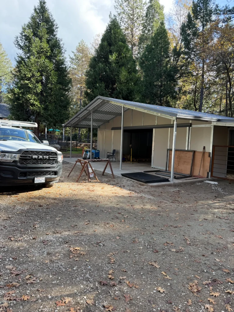 Residential horse barn construction in Foresthill, CA, featuring metal structure, concrete foundation, and surrounding trees, showcasing Ibarra Construction's craftsmanship and attention to detail.