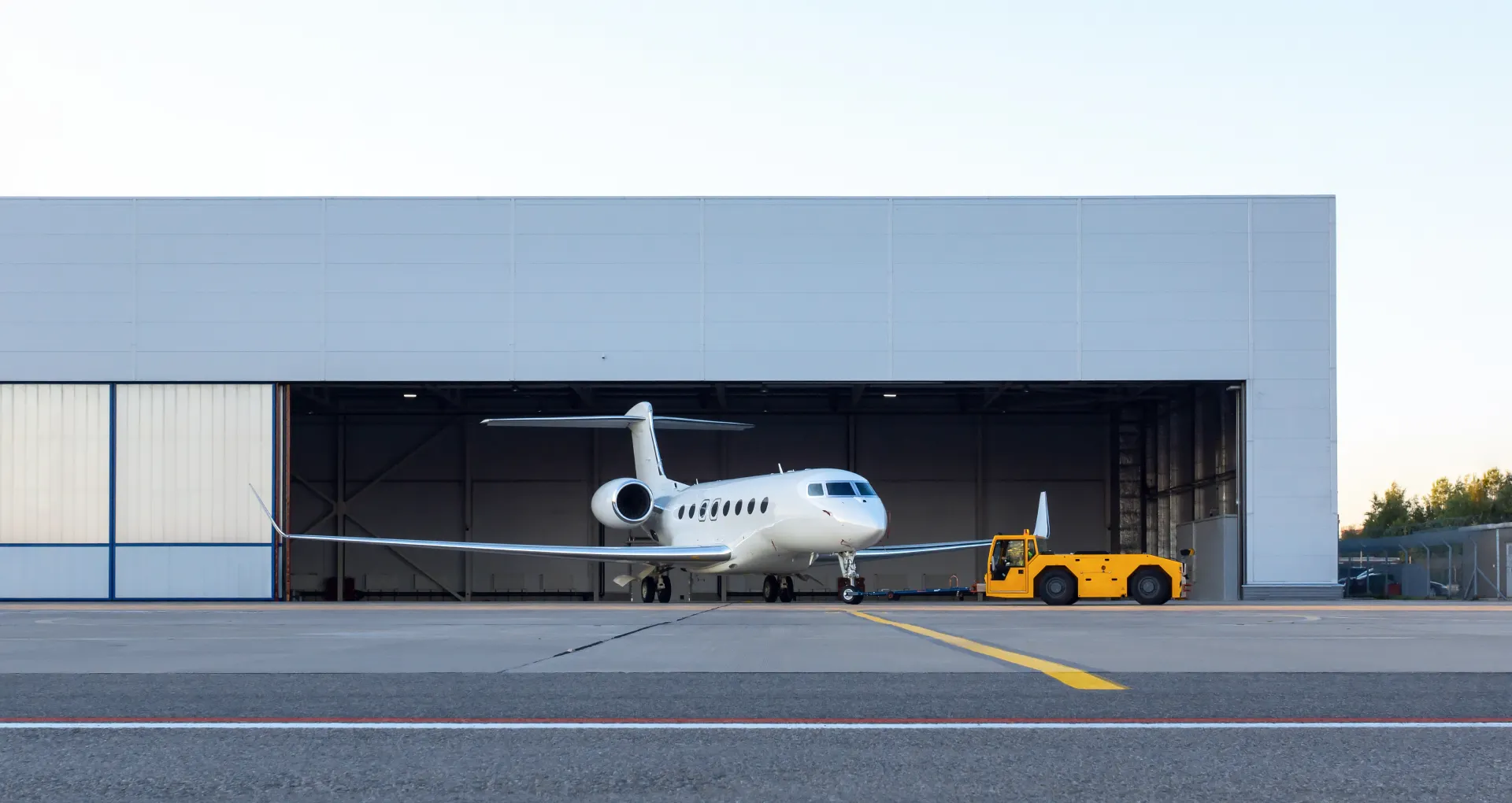 Airplane hangar with a white jet and yellow towing vehicle, showcasing durable construction and maintenance capabilities for aircraft protection.