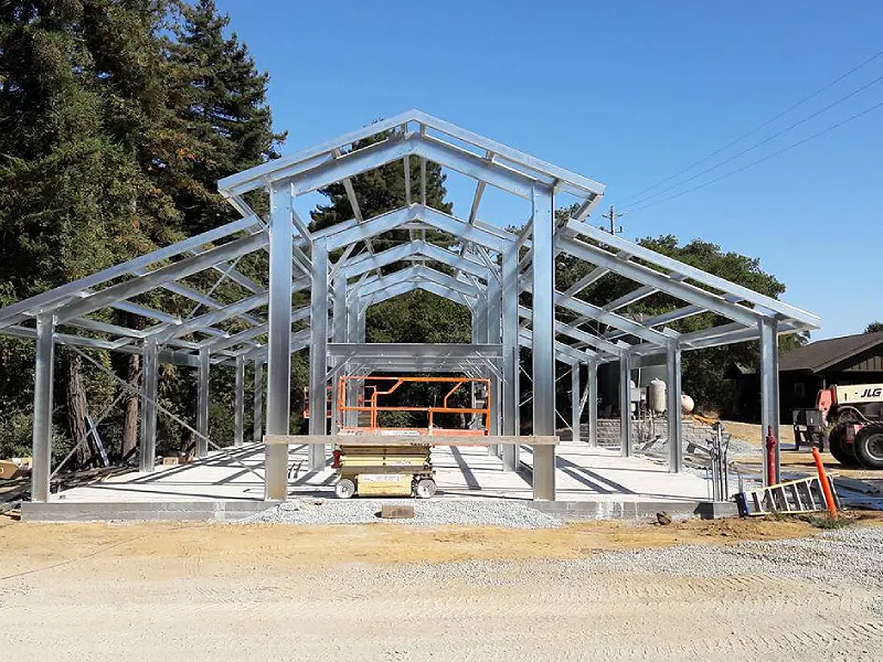 Metal building structure under construction, showcasing steel framework and concrete foundation, with construction equipment in a site preparation context.