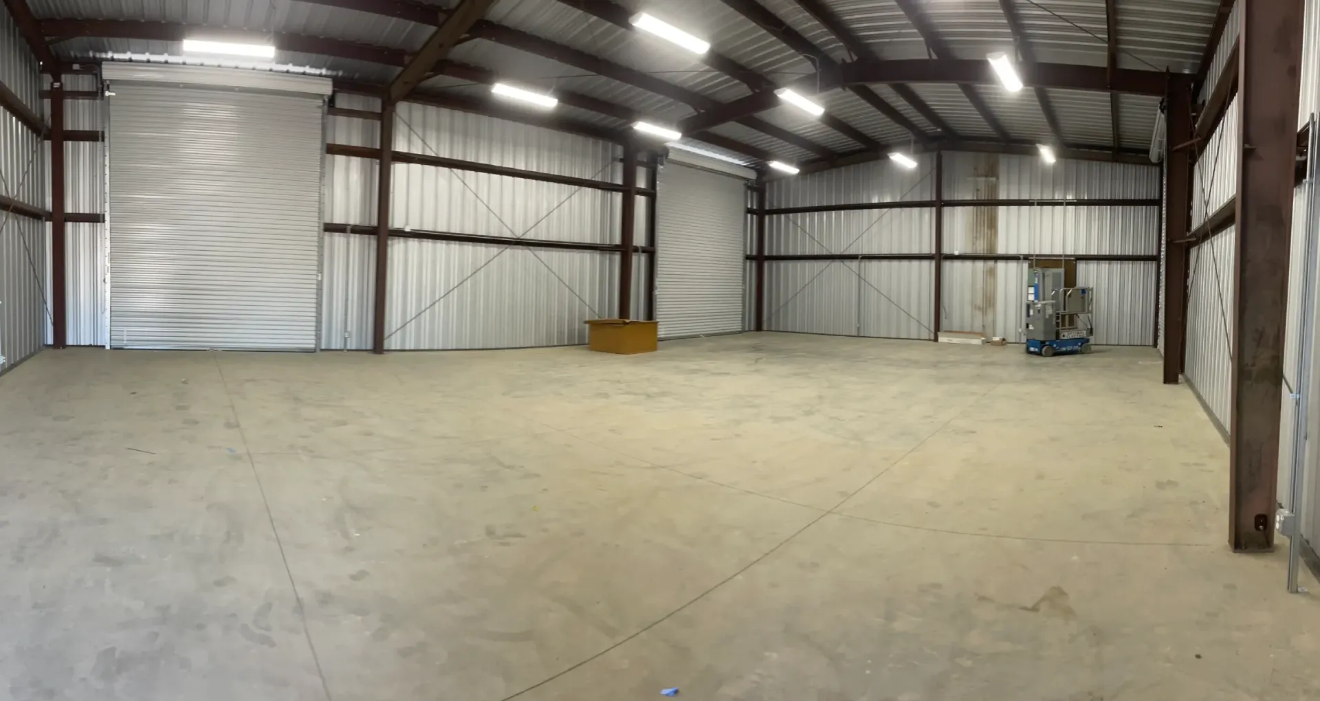 Interior view of a steel commercial structure with a concrete floor, overhead lights, and a large roll-up door, showcasing ample space for agricultural or business use, relevant to Ibarra Construction's specialized services in Woodland, CA.