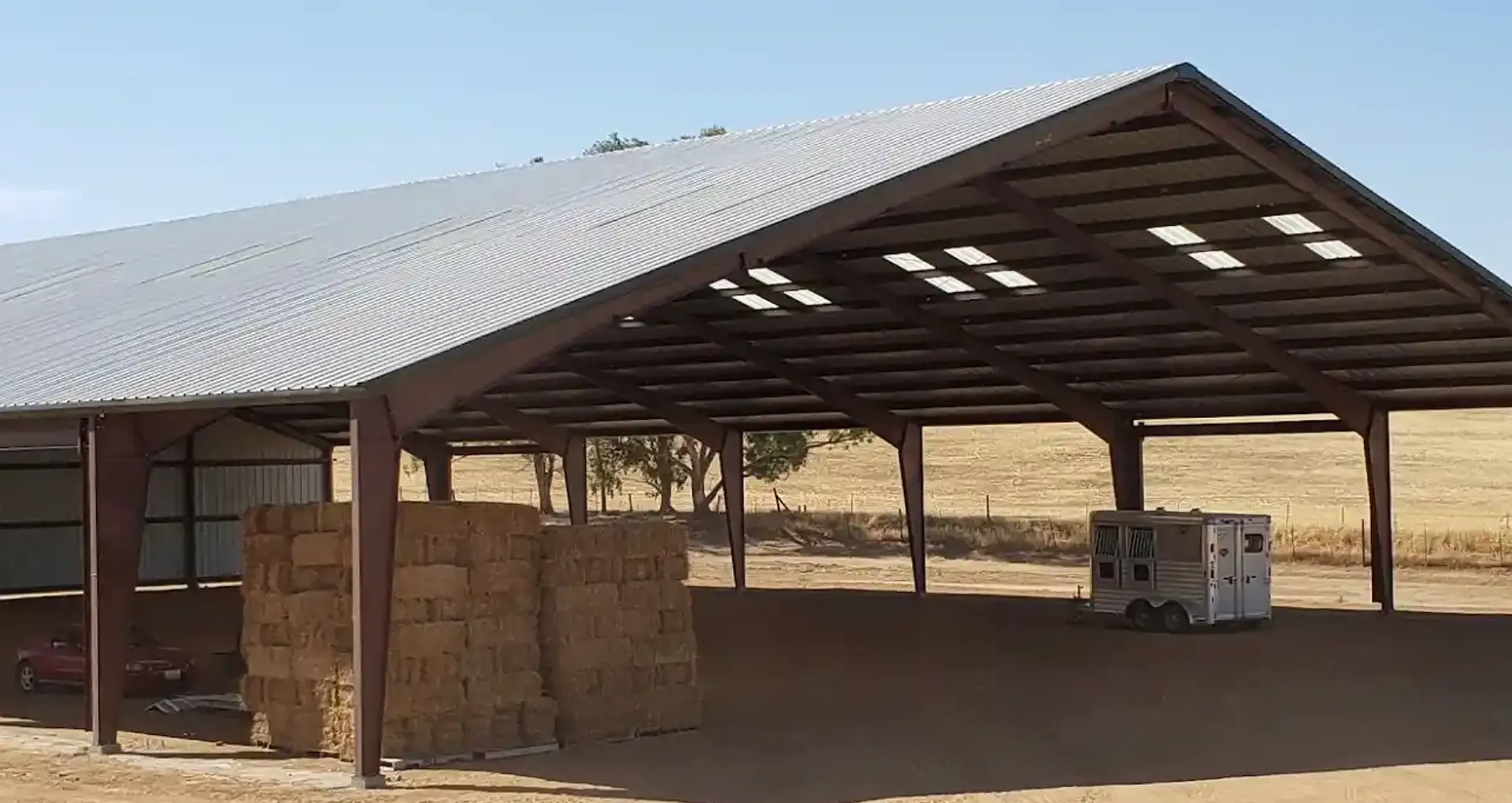 Metal commercial shop featuring a sturdy, rust-resistant steel structure with a peaked roof, showcasing a spacious interior with stacked hay bales and a trailer, designed for agricultural and business use.