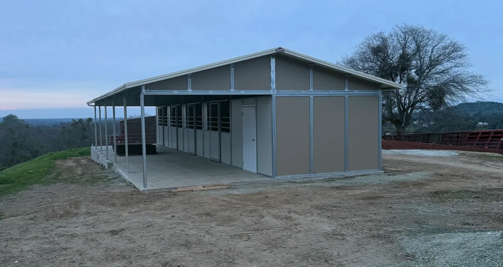 Prefabricated horse barn installation in Valley Springs, CA, showcasing steel structure, covered porch, and surrounding landscape.