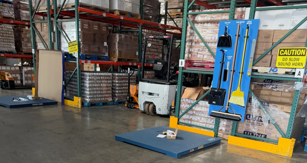 Warehouse interior with concrete scale installation, featuring pallet scales, cleaning tools display, and stacked goods in the background, illustrating commercial modifications for Yolo Food Bank in Woodland, CA.