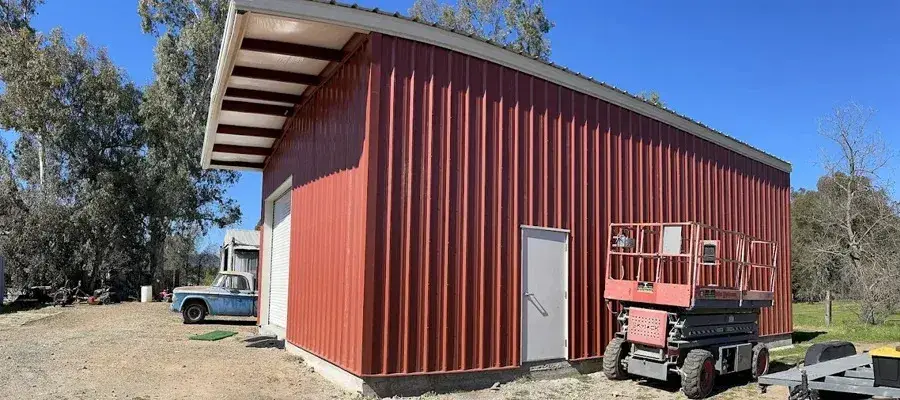 Red metal building with a lift and vintage truck nearby.